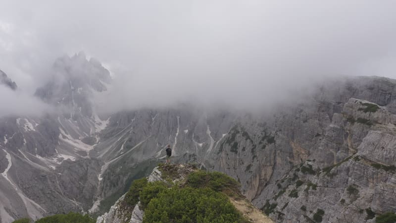 Circling drone shot of figure standing on mountain edge with beautiful cragged peaks in the backdrop, in the Dolomites in Italy