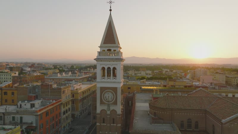 Orbit shot around tower at sunrise. Church, buildings in urban borough and distant mountain in background. Rome, Italy