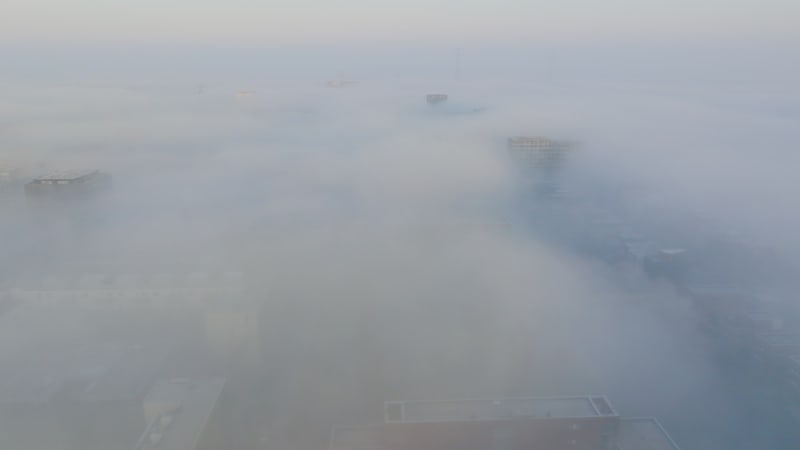 Fly over tall buildings at mist packed city at the edge of Amsterdam during sunrise