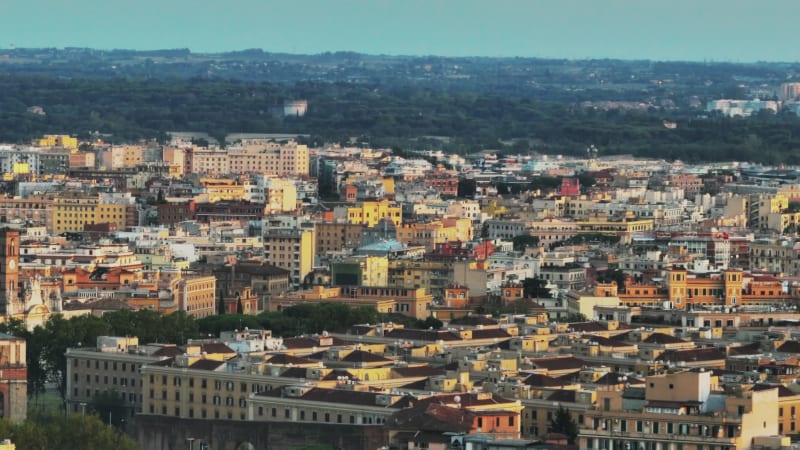 Fly above city. Aerial zoomed shot of apartment buildings in city centre lit by low sun. Rome, Italy