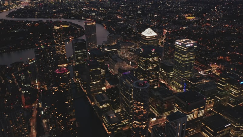 Aerial shot of skyscrapers in futuristic Canary Wharf urban district. Tall office buildings around Canada Square at night. London, UK