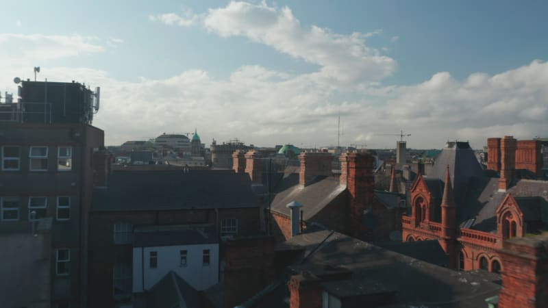 Forwards low flight from parking lot above roofs of historical brick houses with many chimneys. Dublin, Ireland