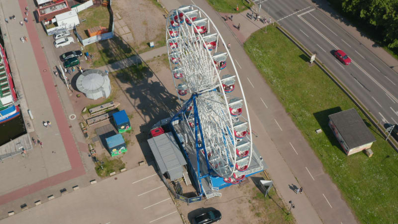 High angle view of rotating Ferris wheel. People enjoying amusement ride in gondolas. Shadow of attraction on ground