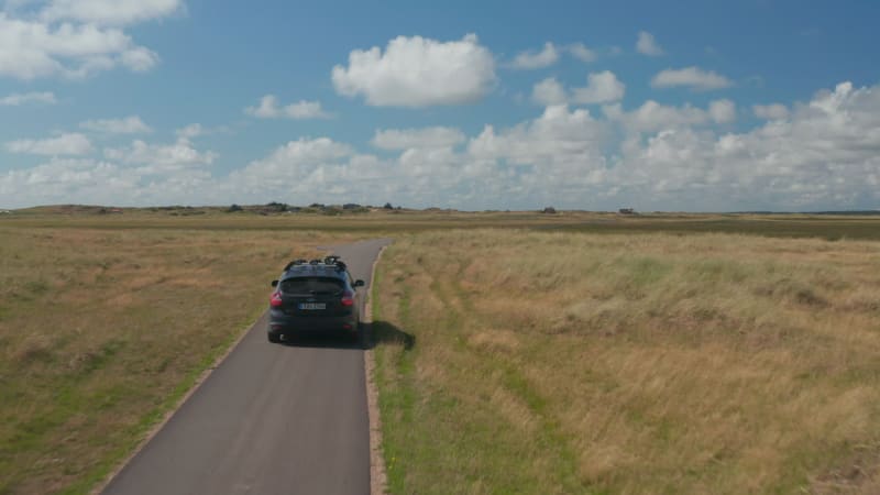 Family car driving on narrow road in countryside. Meadows and pastures with high grass along pathway. Denmark