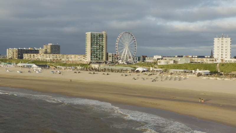 People walking on the beach with ferris wheel in the background.