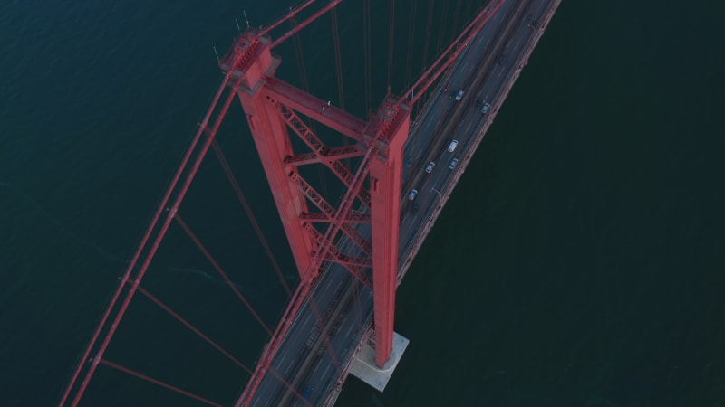 Aerial view of Almada end of 25th of April Bridge. Long cable-stayed highway bridge over Tegus river. Drone camera tilting up. Lisbon, capital of Portugal.