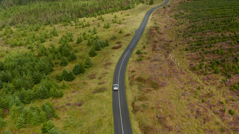 High angle view of sports car driving on road in wooded landscape. Forwards tracking of single vehicle. Ireland