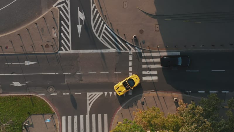 Aerial birds eye overhead top down view of yellow convertible car turning on main road. Late afternoon sunlight with long shadows. Warsaw, Poland