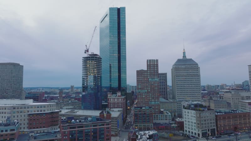 Tall modern glossy glass skyscraper reflecting surrounding construction site. High rise office buildings at dusk. Boston, USA