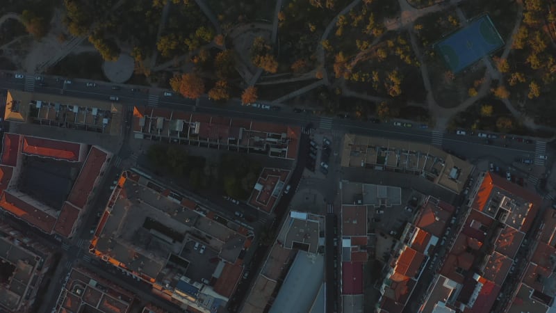 Aerial birds eye overhead top down panning view buildings in urban neighbourhood and public park at sunset.