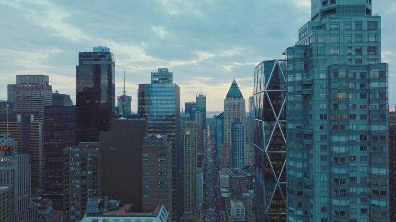 Forwards fly along row of modern tall buildings. Upper storeys of skyscrapers high above streets. View against sky at twilight. Manhattan, New York City, USA