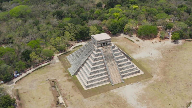 Aerial pull back footage of old Maya town site. Big stone pyramid of temple and several smaller buildings. Historical monuments of pre-Columbian era, Chichen Itza, Mexico.