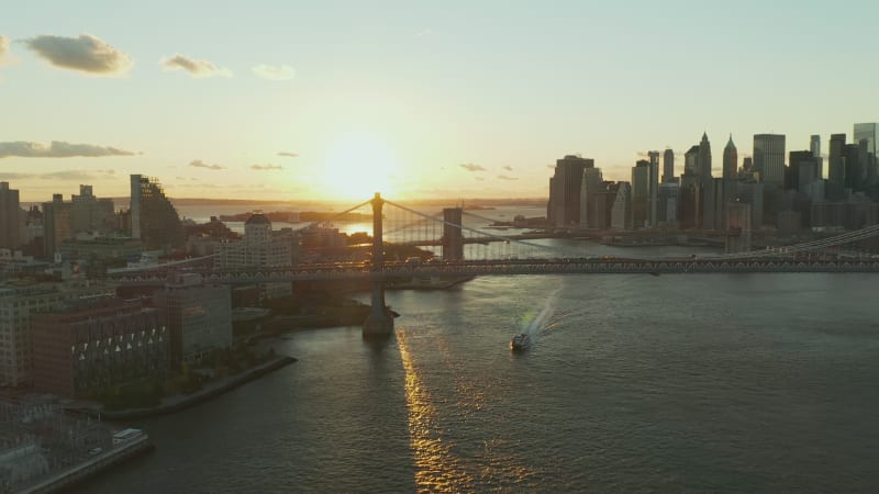 Breath taking aerial view of cruise ship passing under Manhattan Bridge at sunset. Downtown skyscrapers on waterfront in background. Manhattan, New York City, USA