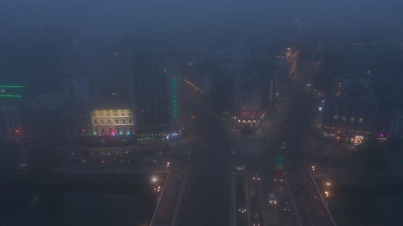 Aerial sliding view of embankment and vehicles driving on OConnell Bridge. Limited visibility due to foggy weather. Dublin, Ireland