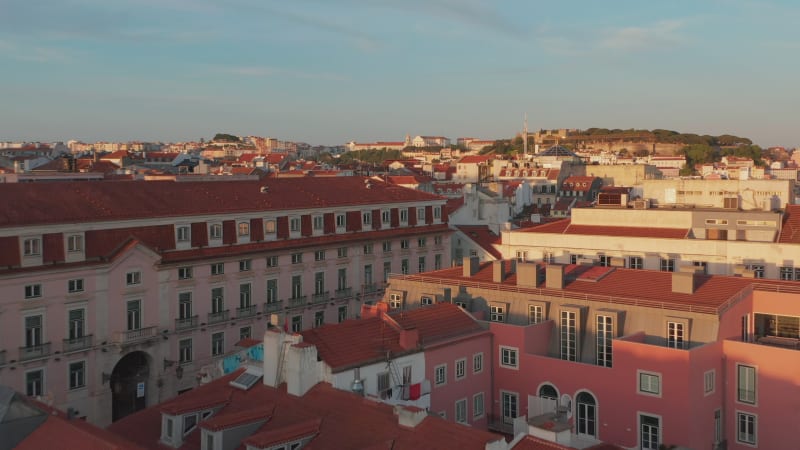 Elevated evening view of bright sun illuminated buildings downtown. Drone flying over red rooftops. Lisbon, capital of Portugal.