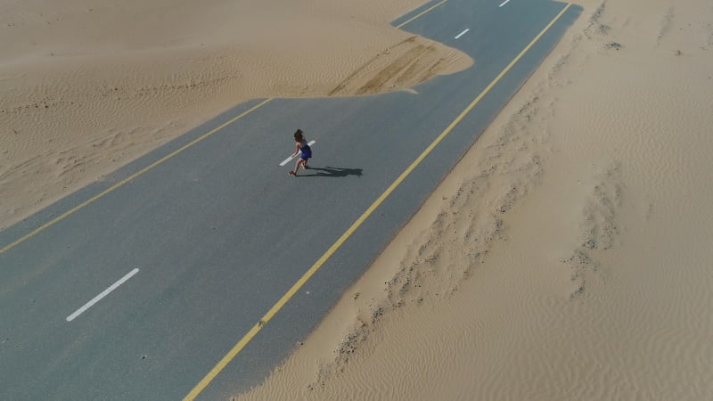 Aerial view of woman doing exercise in road cover by sand on Abu Dhabi