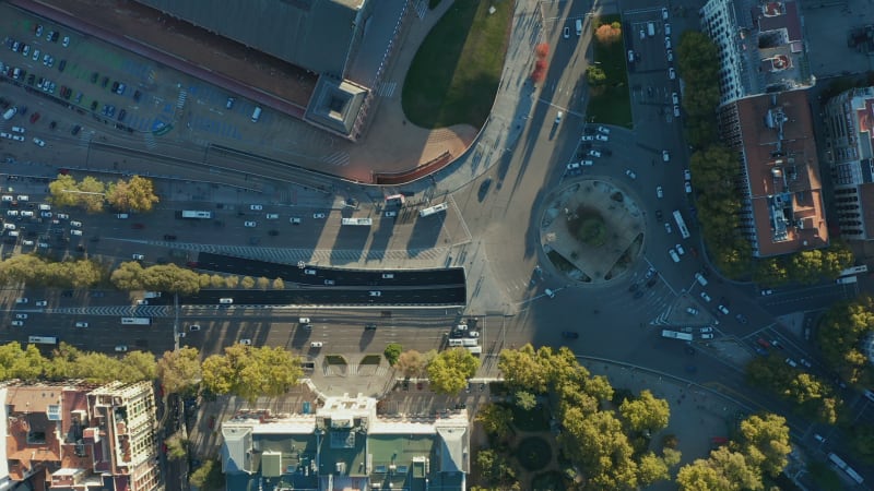 Aerial birds eye overhead top down ascending shot of traffic on roundabout and surrounding multilane roads in city.