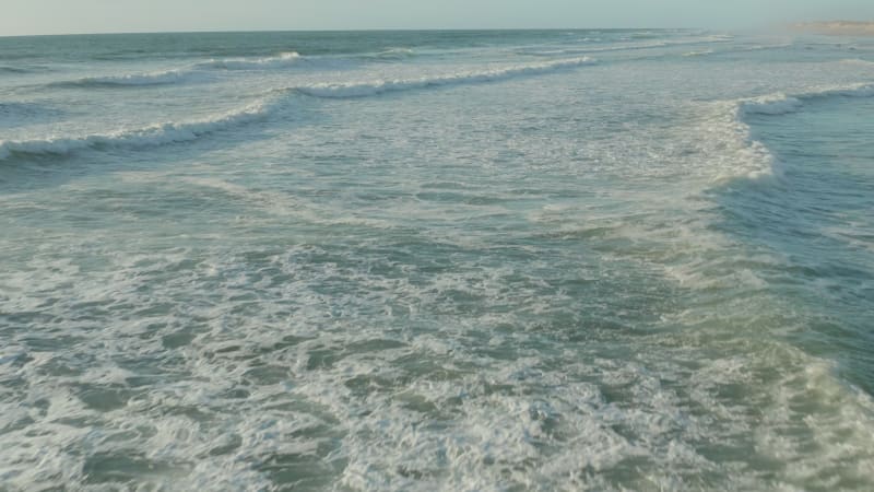 Perfect Waves with white Foam in beautiful afternoon light and clear Sky, Aerial low angle forward dolly