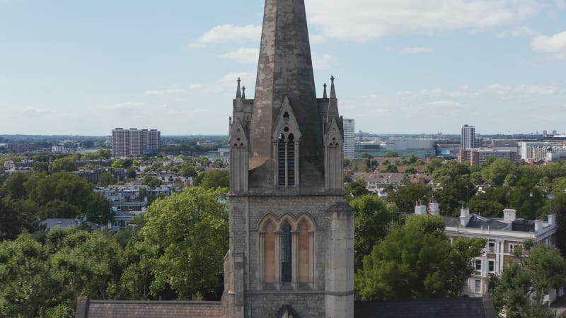 Forwards fly towards tower of gothic church. Closeup view of arches and decoration of spire. Historic building surrounded by trees in town. London, UK