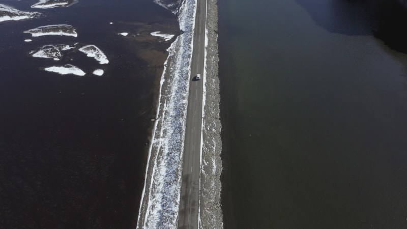 Car Driving Along a Narrow Road Crossing a Lake in Iceland