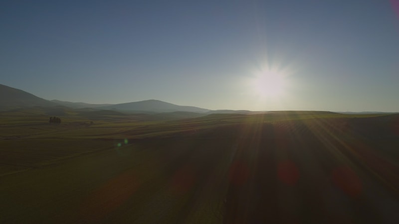 Aerial view of beautiful hills with lots of grass and the sun shining.