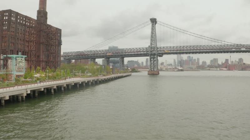 Establishing Shot forward Dolly under Williamsburg Bridge next to Old Rusty Warehouse on Overcast Day with Cloudy Sky