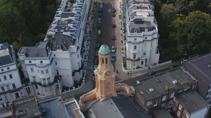 Descending closeup view of church clock tower. Tilt up revealing street with white houses. London, UK