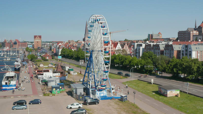 Rising view of running Ferris wheel. People enjoying time on attraction. Ascending and tilting down footage with city in background