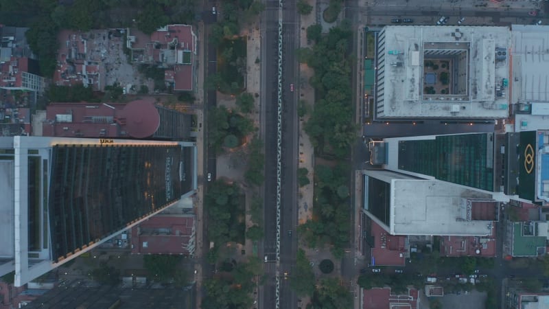 Aerial ascending overhead birds eye view of cars driving on the street surrounded by skyscrapers in urban city center of Mexico City