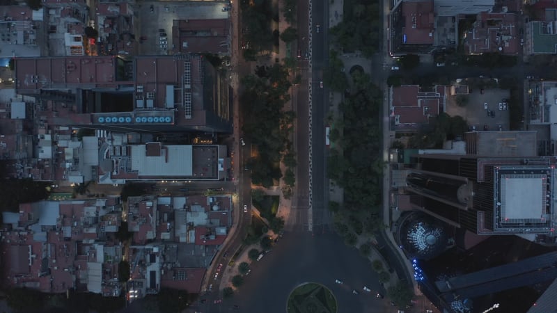 Aerial birds eye overhead top down panning view of traffic on wide street with circular crossroad. Flying drone following road in evening. Mexico city, Mexico.