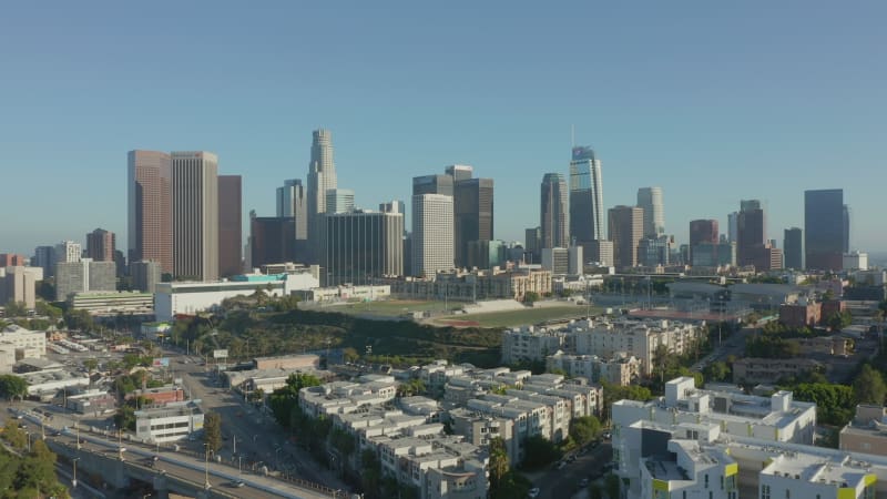 Flying towards Downtown Los Angeles, California Skyline with sports football baseball and tennis field at beautiful blue sky and sunny day