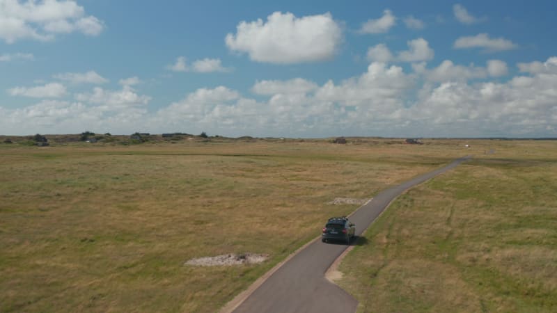 Tracking of car driving on narrow asphalt road surrounded by grassland and meadows. Flat green landscape on sunny day. Denmark