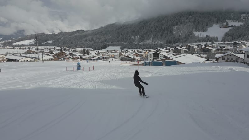 Snowboarder's Journey into Flachau Village low-flying aerial shot