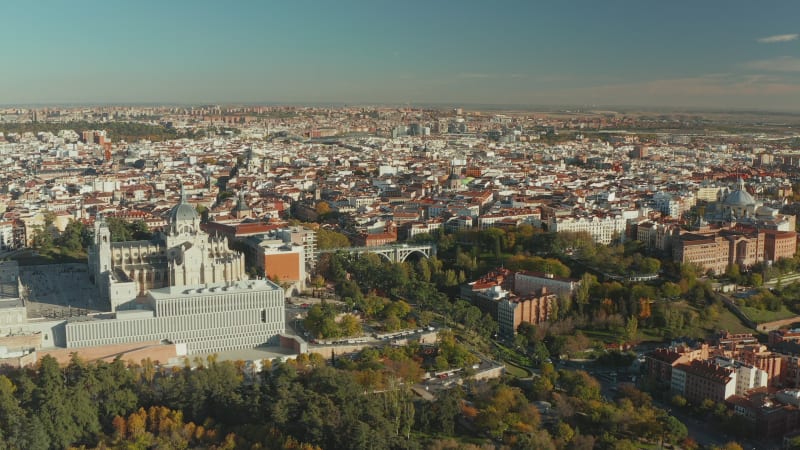 Forwards fly above town park. Aerial view of large city with historic landmarks. Almudena Cathedral above valley spanned by Segovia Viaduct.