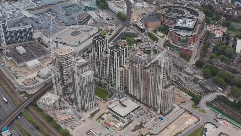 Slide and pan footage of tower cranes on construction site of apartment buildings complex. Aerial view of modern city district. London, UK