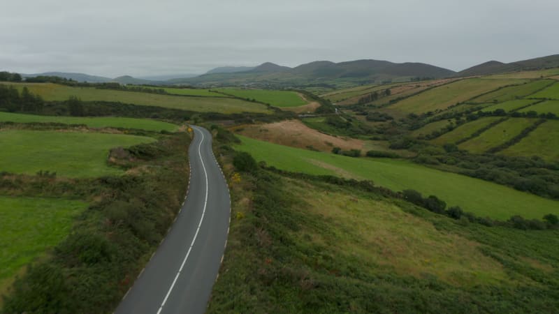 Forwards fly above road in countryside. Cloudy day in landscape with green meadow and pastures. Ireland