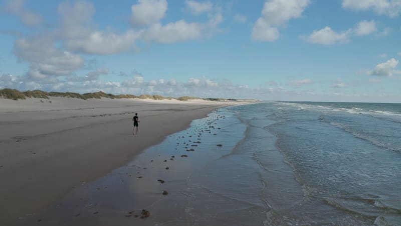 Running on beach along coast. Barefoot sportsman jogging on sand surface. Mild waves rolling to bank. Denmark