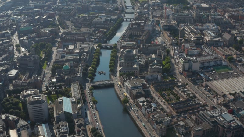 Forwards fly high above River Liffey calmly flowing in city. Traffic on embankment roads. Dublin, Ireland