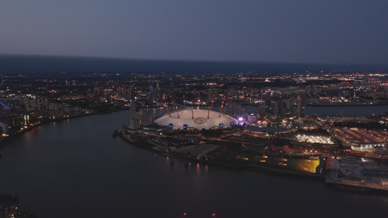 Evening aerial view of Millennium Dome. O2 arena at night. Illuminated city streets and buildings. London, UK