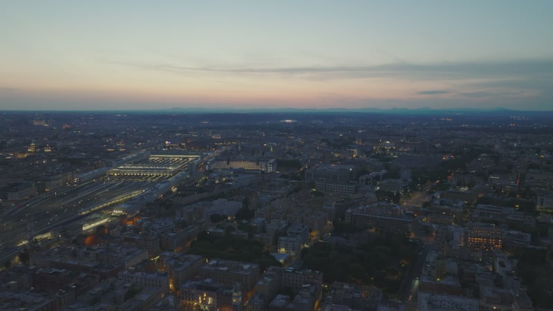 Aerial panoramic view of evening city and colour twilight sky in background. Richly illuminated central train station. Rome, Italy