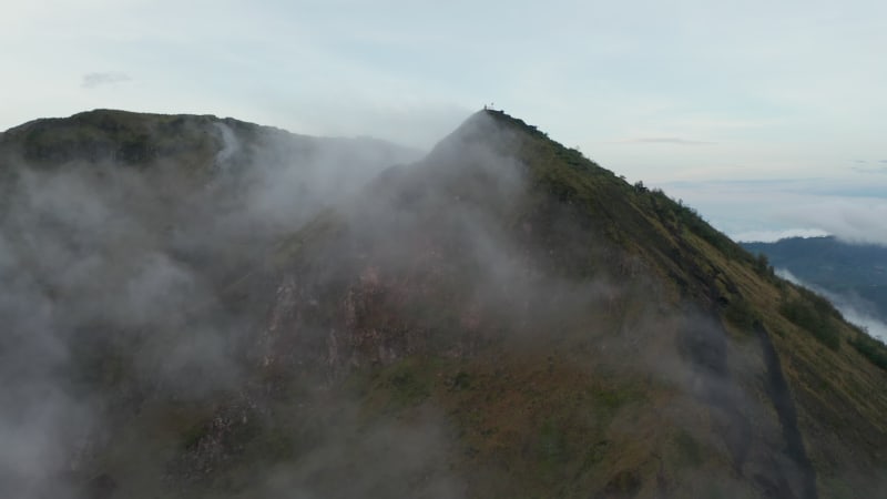 Aerial truck shot flying past the mountain top of an active volcano in tropical climate and disappearing into the fog