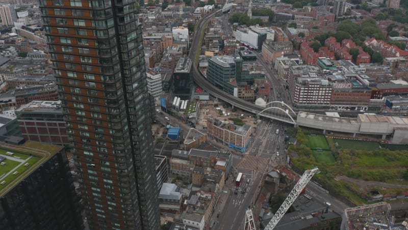 Forwards fly above city. Tilt down on road intersection and railway bridge over street. Vehicles driving n roads. London, UK