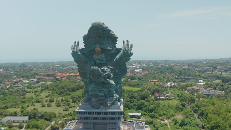 Circling a majestic Garuda Wisnu Kencana statue in Bali, Indonesia. Huge religious monument sculpture of Vishnu riding Garuda rising above the city