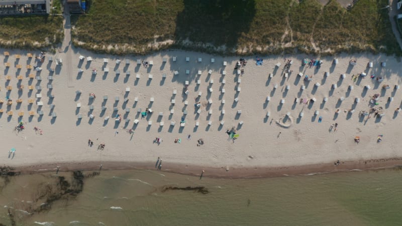 Aerial birds eye overhead top down view of tourist beach in Scharbeutz, Germany, with beach chairs and people sunbathing, sideways, sunny day