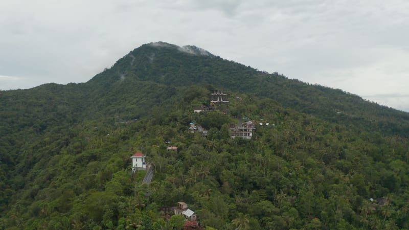 Aerial view of Hindu temple and rural houses at the foot of a mountain in Bali. Pura Penataran Agung Lempuyang temple and residential homes on the slopes of mountain Lempuyang