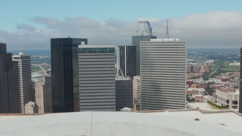 Low flight above flat roof of tall office building. Forwards reveal of group of modern downtown skyscrapers. Dallas, Texas, US