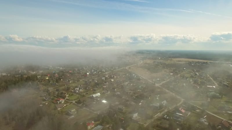 Aerial view of small town with houses and a misty forest.