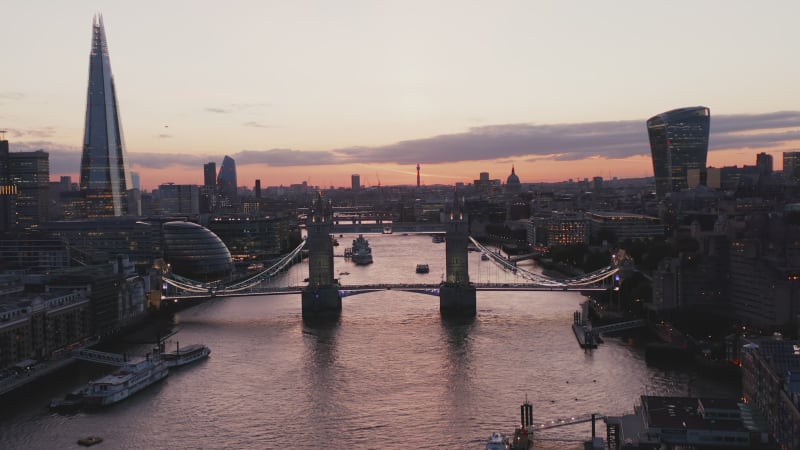 Ascending footage of bridges across Thames river against twilight sky. Illuminated famous Tower Bridge in foreground. London, UK