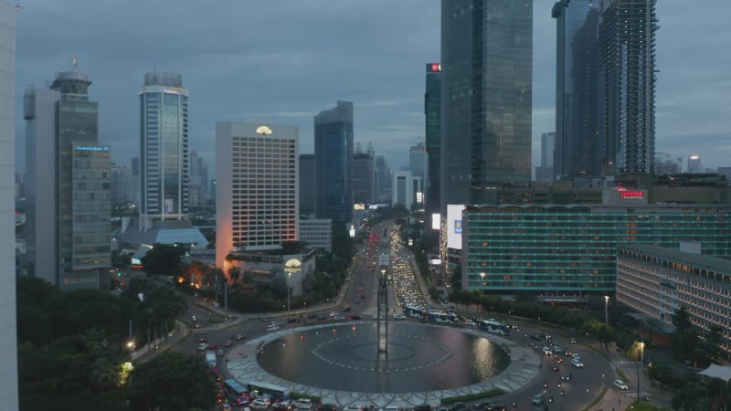 Aerial dolly shot of busy rush hour traffic in large roundabout surrounded by skyscrapers in Jakarta, Indonesia