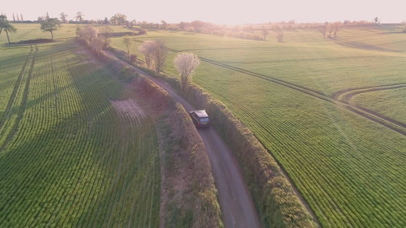 Aerial View of a Luxury SUV Driving Through a Country Lane in the Evening